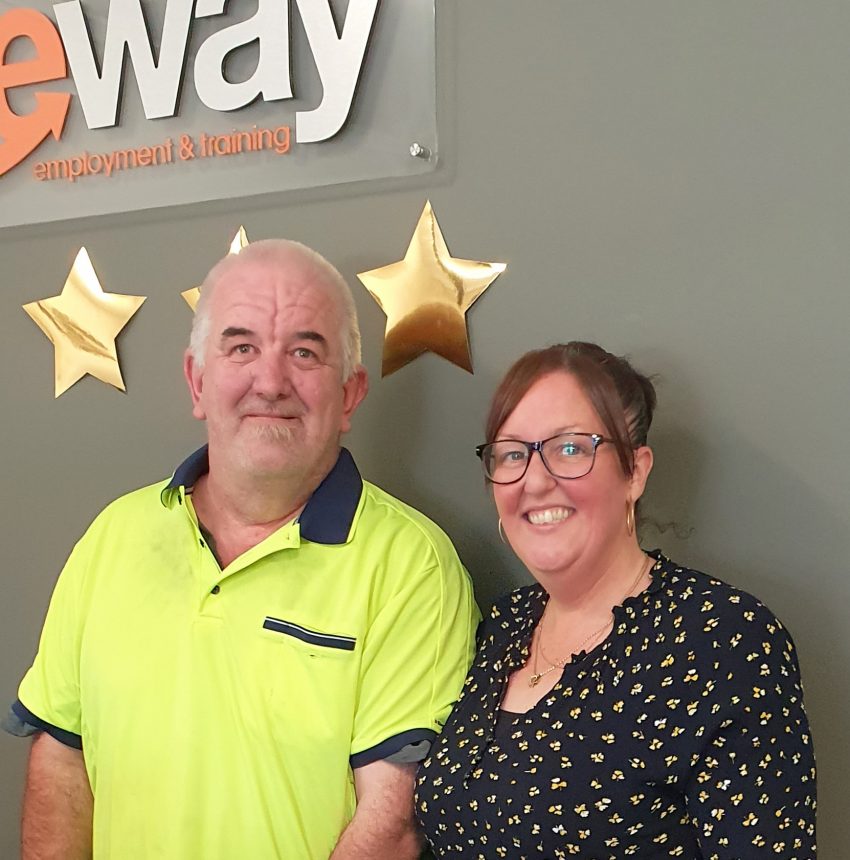Sean wears his yellow high viz work shirt while he stands next to his Sureway consultant smiling